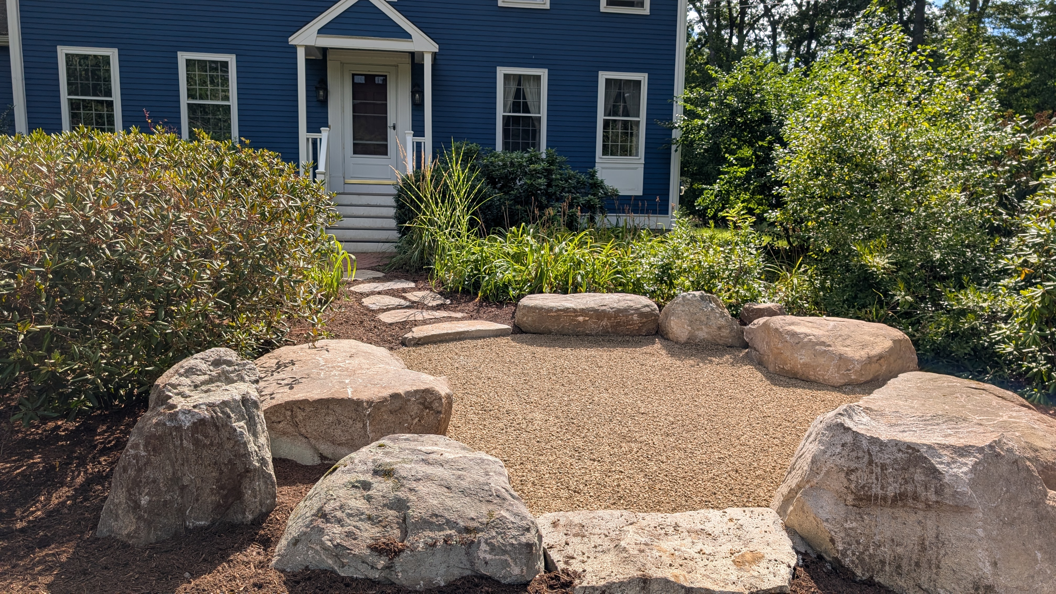 Boulder circle garden with gravel center and blue colonial house